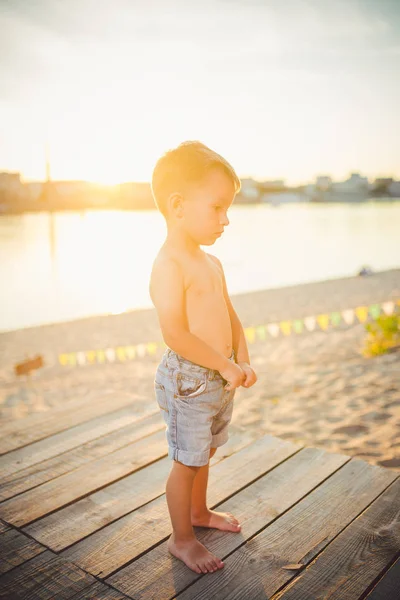 Niño pequeño caucásico sentado en la playa de arena del muelle de madera, hora de verano, vacaciones de mar cerca del agua. El tema es el flujo del tiempo, una vida corta, el significado y el propósito de la existencia. Significado de la vida —  Fotos de Stock