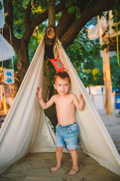 Thema Sommerurlaub, kleiner Junge, kaukasisches Kind, das im Waldgebiet im Park auf dem Spielplatz im Hof spielt. Kind im tipi wigwam Zelt im Sommer. Erkunden und Spielen in der Natur zur Sommerzeit — Stockfoto