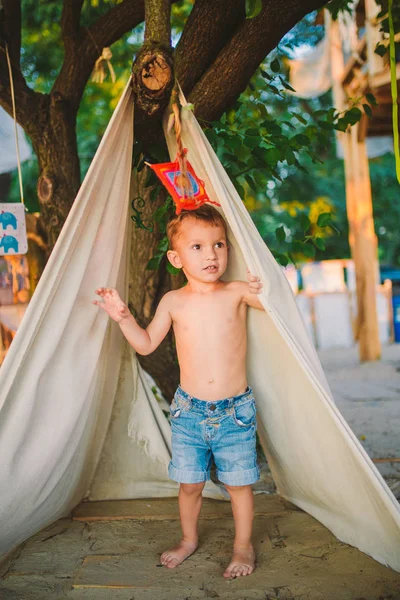 Tema férias de verão, menino, criança caucasiana brincando na área arborizada no parque no playground no quintal. miúdo em Tipi wigwam tenda no verão. Explore e jogue na natureza na hora de verão — Fotografia de Stock