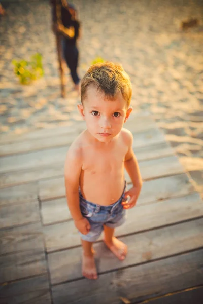 Niño pequeño caucásico sentado en la playa de arena del muelle de madera, hora de verano, vacaciones de mar cerca del agua. El tema es el flujo del tiempo, una vida corta, el significado y el propósito de la existencia. Significado de la vida —  Fotos de Stock