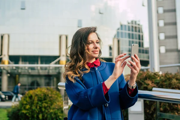 Edifici per uffici gente di città in giacca e cravatta. Donna d'affari caucasica utilizzando smartphone con mano. Concetto aziendale. Ritratto elegante donna d'affari in abiti alla moda che tiene il telefono vicino all'edificio dell'ufficio — Foto Stock