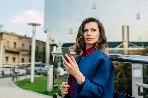 Edificios de oficinas gente de ciudad en traje. Mujer de negocios caucásica usando teléfono inteligente con la mano. Concepto de negocio. Retrato mujer de negocios con estilo en la ropa de moda celebración de teléfono cerca del edificio de oficinas —  Fotos de Stock