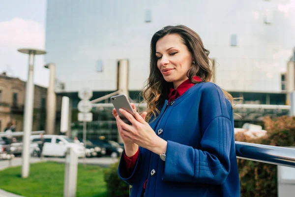 Edifici per uffici gente di città in giacca e cravatta. Donna d'affari caucasica utilizzando smartphone con mano. Concetto aziendale. Ritratto elegante donna d'affari in abiti alla moda che tiene il telefono vicino all'edificio dell'ufficio — Foto Stock