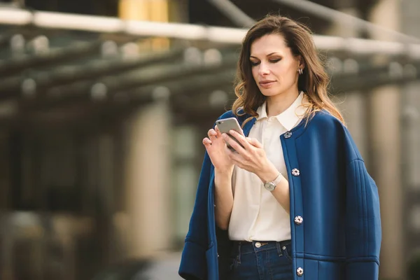 Edifici per uffici gente di città in giacca e cravatta. Donna d'affari caucasica utilizzando smartphone con mano. Concetto aziendale. Ritratto elegante donna d'affari in abiti alla moda che tiene il telefono vicino all'edificio dell'ufficio — Foto Stock