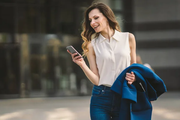 Edifici per uffici gente di città in giacca e cravatta. Donna d'affari caucasica utilizzando smartphone con mano. Concetto aziendale. Ritratto elegante donna d'affari in abiti alla moda che tiene il telefono vicino all'edificio dell'ufficio — Foto Stock