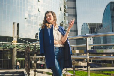 Ofis binaları şehir insanları takım elbiseli. Beyaz iş kadını el ile akıllı telefon kullanıyor. İş konsepti. Ofis binası yakınında Telefon tutan şık giysiler Portre şık iş kadını