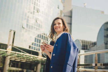 Ofis binaları şehir insanları takım elbiseli. Beyaz iş kadını el ile akıllı telefon kullanıyor. İş konsepti. Ofis binası yakınında Telefon tutan şık giysiler Portre şık iş kadını