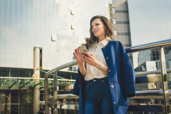 Edifícios de escritórios pessoas da cidade de terno. Mulher de negócios caucasiana usando smartphone com a mão. Conceito de negócio. Retrato mulher de negócios elegante em roupas elegantes segurando telefone perto de prédio de escritórios — Fotografia de Stock