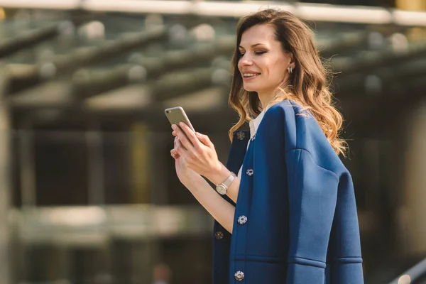 Edifici per uffici gente di città in giacca e cravatta. Donna d'affari caucasica utilizzando smartphone con mano. Concetto aziendale. Ritratto elegante donna d'affari in abiti alla moda che tiene il telefono vicino all'edificio dell'ufficio — Foto Stock