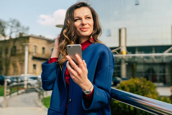 Edifici per uffici gente di città in giacca e cravatta. Donna d'affari caucasica utilizzando smartphone con mano. Concetto aziendale. Ritratto elegante donna d'affari in abiti alla moda che tiene il telefono vicino all'edificio dell'ufficio — Foto Stock