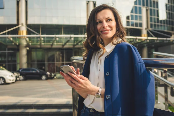 Edifícios de escritórios pessoas da cidade de terno. Mulher de negócios caucasiana usando smartphone com a mão. Conceito de negócio. Retrato mulher de negócios elegante em roupas elegantes segurando telefone perto de prédio de escritórios — Fotografia de Stock