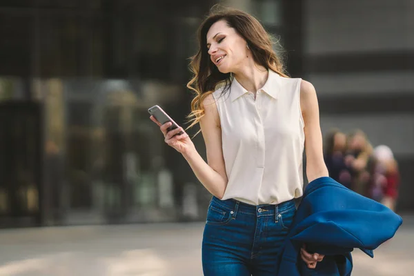 Edifici per uffici gente di città in giacca e cravatta. Donna d'affari caucasica utilizzando smartphone con mano. Concetto aziendale. Ritratto elegante donna d'affari in abiti alla moda che tiene il telefono vicino all'edificio dell'ufficio — Foto Stock