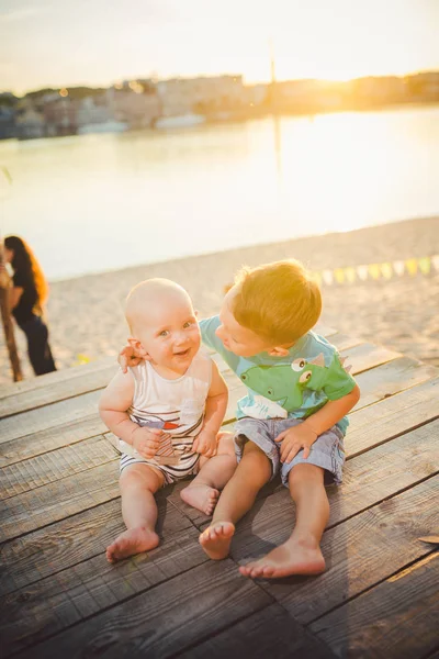 Dos niñitos sentados en el muelle de la orilla del río. Concepto de amistad y fraternidad. Soleado y alegre día de verano. Niños sentados en el muelle. Dos niños de diferentes edades sentados en un muelle de madera —  Fotos de Stock