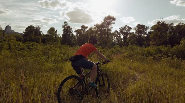 Joven atlética mujer caucásica montando bicicletas de montaña en el hermoso campo de hierba de plumas. Aventura y viajes. Bicicleta deportiva, Ciclismo en el hermoso prado. ciclista en bicicleta en el paisaje natural — Foto de Stock