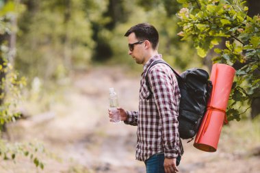 Ormanda Yürüyüşçü İçme Suyu. Yorgun adam ormanlık alanda şişeden su içiyor. Sırt Çantası ve Ormanda Flask ile Yakışıklı Traveler. tatil, açık yaşam tarzı özgürlük kavramı. Maceralar yürüyüş