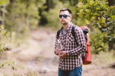 Ormanda Yürüyüşçü İçme Suyu. Yorgun adam ormanlık alanda şişeden su içiyor. Sırt Çantası ve Ormanda Flask ile Yakışıklı Traveler. tatil, açık yaşam tarzı özgürlük kavramı. Maceralar yürüyüş
