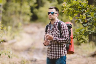 Ormanda Yürüyüşçü İçme Suyu. Yorgun adam ormanlık alanda şişeden su içiyor. Sırt Çantası ve Ormanda Flask ile Yakışıklı Traveler. tatil, açık yaşam tarzı özgürlük kavramı. Maceralar yürüyüş