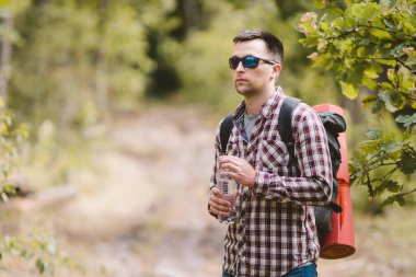 Ormanda Yürüyüşçü İçme Suyu. Yorgun adam ormanlık alanda şişeden su içiyor. Sırt Çantası ve Ormanda Flask ile Yakışıklı Traveler. tatil, açık yaşam tarzı özgürlük kavramı. Maceralar yürüyüş