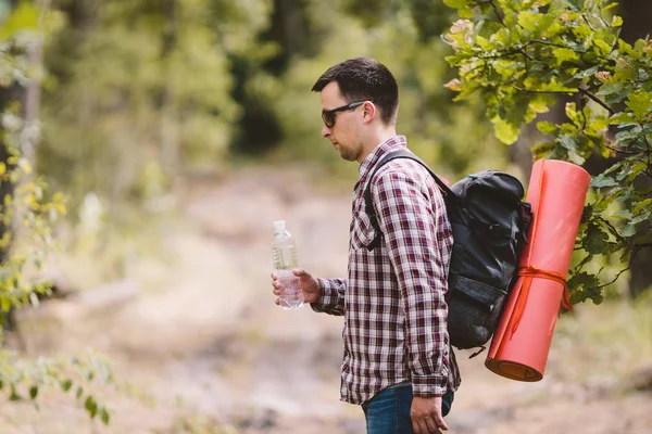 Ormanda Yürüyüşçü İçme Suyu. Yorgun adam ormanlık alanda şişeden su içiyor. Sırt Çantası ve Ormanda Flask ile Yakışıklı Traveler. tatil, açık yaşam tarzı özgürlük kavramı. Maceralar yürüyüş