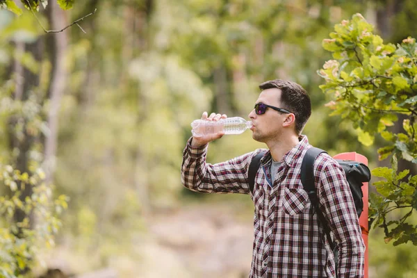 Caminhante água potável na floresta. Cansado de beber água da garrafa na floresta. Viajante bonito com mochila e frasco na floresta. férias, conceito de liberdade ao ar livre estilo de vida. Aventuras caminhadas — Fotografia de Stock