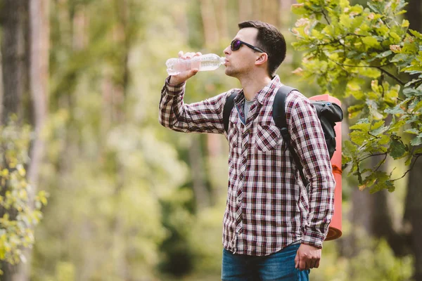 Caminhante água potável na floresta. Cansado de beber água da garrafa na floresta. Viajante bonito com mochila e frasco na floresta. férias, conceito de liberdade ao ar livre estilo de vida. Aventuras caminhadas — Fotografia de Stock