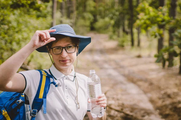 Descontraído turista feminino descansando na natureza. Mulher feliz turista com mochila. menina turista água potável na floresta. Mulher com garrafa. Atraente turista refrescar beber água após viagem mochileiro — Fotografia de Stock