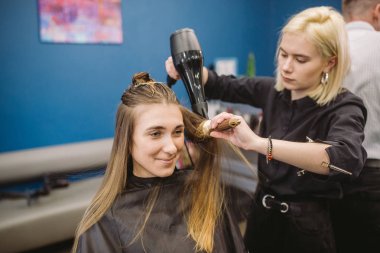 Kuaförde mutlu kadının portresi. Profesyonel saç şekillendirme konsepti. Kuaför saç kurutma makinesi ve fırça kullanarak kız uzun saç kurutma. Fön Kurutma Makinesi ile Kurutma