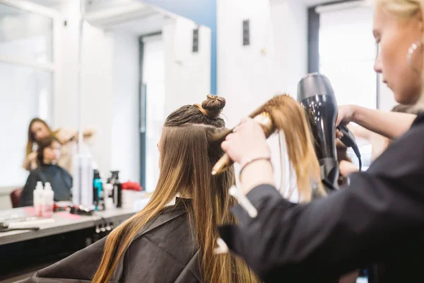 Portret van gelukkige vrouw in de kapsalon. Professioneel haar styling concept. Kapper drogen meisje lang haar met behulp van haardroger en borstel. Drogen met föhn — Stockfoto