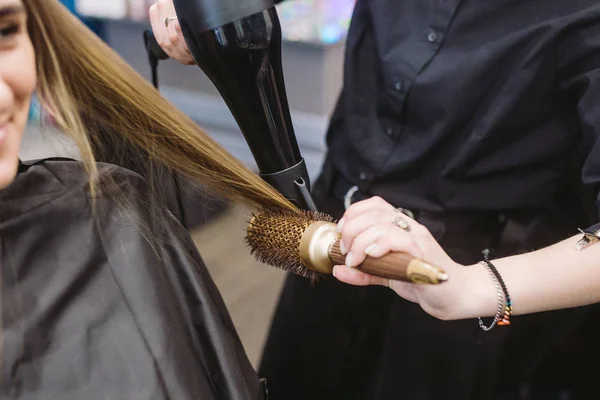 Portret van gelukkige vrouw in de kapsalon. Professioneel haar styling concept. Kapper drogen meisje lang haar met behulp van haardroger en borstel. Drogen met föhn — Stockfoto