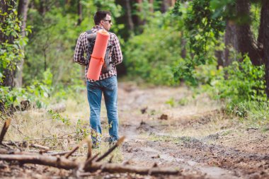 Kavram nefes kesen yolculuk ve macera. Sırt çantası ile geri görünüm yürüyüş cesur Kafkas adam kırsal yol boyunca ormana yürüyor. Tema turizm ve açık hava etkinlikleri. backpacker orman geçer