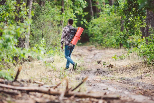 Concept breathtaking journey and adventure. Back view hike brave Caucasian guy with backpack walks into forest along country road. Theme tourism and outdoor activities. backpacker goes through forest