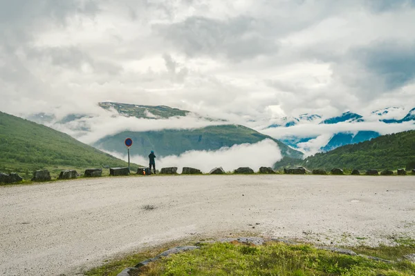 Człowiek w kasku fotograf robienia zdjęć z powrotem widok gór krajobraz w deszczowej pogody w Norwegii. Podróże Lifestyle. Wanderlust przygoda koncepcja wakacje na zewnątrz w The dziki — Darmowe zdjęcie stockowe