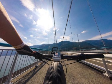 İskandinavya'da dağ bisikleti teması. Norveç'te Bisikletli kask lı ve spor giyimli insan turist, Norveç'in güneybatısındaki Hardanger Fjord'a atılan Hardanger Köprüsü asma köprüsünde