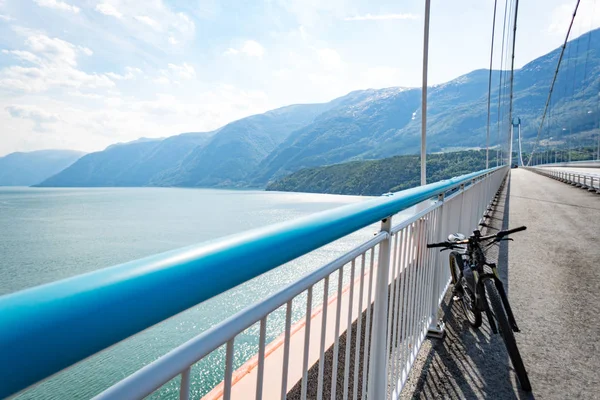 Theme of mountain biking in Scandinavia. human tourist in helmet and sportswear on bicycle in Norway on Hardanger Bridge suspension bridge thrown across the Hardanger Fjord in southwestern Norway — Stock Photo, Image