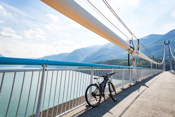 Tema de ciclismo de montaña en Escandinavia. turista humano en casco y ropa deportiva en bicicleta en Noruega en el puente colgante Hardanger Bridge lanzado a través del fiordo Hardanger en el suroeste de Noruega — Foto de Stock