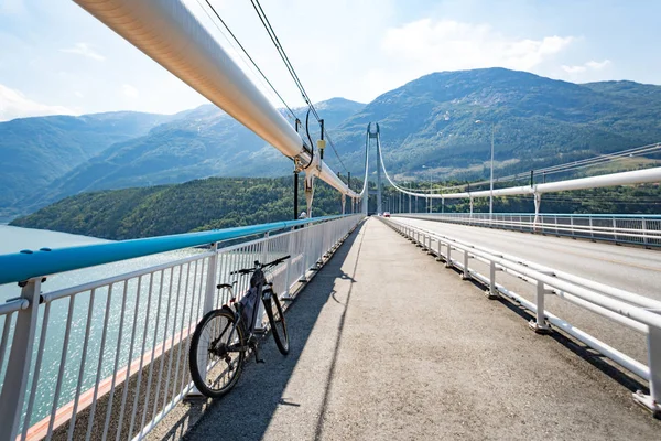 Theme of mountain biking in Scandinavia. human tourist in helmet and sportswear on bicycle in Norway on Hardanger Bridge suspension bridge thrown across the Hardanger Fjord in southwestern Norway — Stock Photo, Image