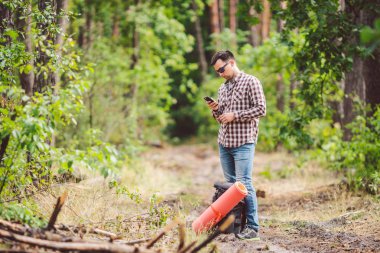 Güzel doğada akıllı telefon kullanarak sırt çantası ile Hipster genç adam. Seyahat konsepti. Açık hava yolculuğu. Seyahat ve keşfetmek. Backpacker erkek orman Gps Route going. Cep telefonu kullanarak portre yürüyüşçü