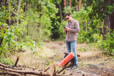 Güzel doğada akıllı telefon kullanarak sırt çantası ile Hipster genç adam. Seyahat konsepti. Açık hava yolculuğu. Seyahat ve keşfetmek. Backpacker erkek orman Gps Route going. Cep telefonu kullanarak portre yürüyüşçü