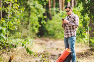 Güzel doğada akıllı telefon kullanarak sırt çantası ile Hipster genç adam. Seyahat konsepti. Açık hava yolculuğu. Seyahat ve keşfetmek. Backpacker erkek orman Gps Route going. Cep telefonu kullanarak portre yürüyüşçü