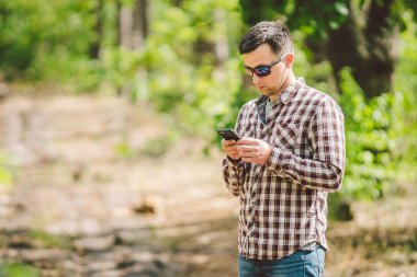 Güzel doğada akıllı telefon kullanarak sırt çantası ile Hipster genç adam. Seyahat konsepti. Açık hava yolculuğu. Seyahat ve keşfetmek. Backpacker erkek orman Gps Route going. Cep telefonu kullanarak portre yürüyüşçü