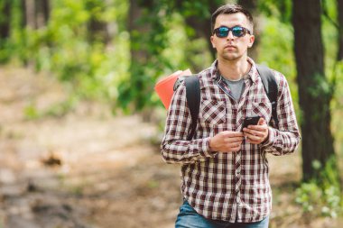 Güzel doğada akıllı telefon kullanarak sırt çantası ile Hipster genç adam. Seyahat konsepti. Açık hava yolculuğu. Seyahat ve keşfetmek. Backpacker erkek orman Gps Route going. Cep telefonu kullanarak portre yürüyüşçü