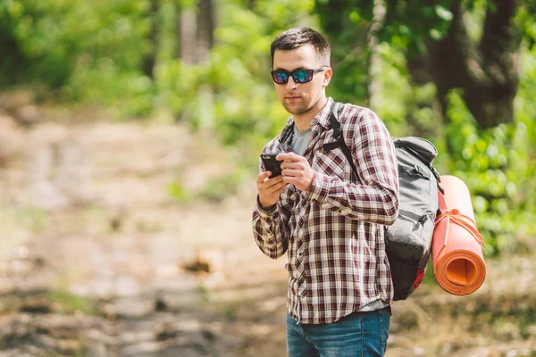 Hipster młody człowiek z plecaka za pomocą inteligentnego telefonu na pięknej przyrody. Koncepcja podróży. Podróże na zewnątrz. Podróżuj i odkrywaj. Backpacker mężczyzna idąc w lesie trasa GPS. Portret Hiker za pomocą telefonu komórkowego — Zdjęcie stockowe