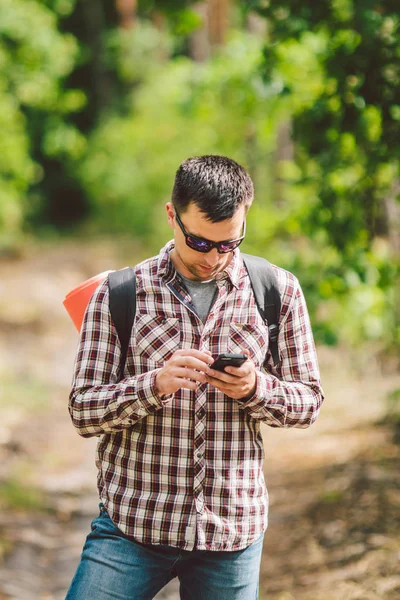 Hipster młody człowiek z plecaka za pomocą inteligentnego telefonu na pięknej przyrody. Koncepcja podróży. Podróże na zewnątrz. Podróżuj i odkrywaj. Backpacker mężczyzna idąc w lesie trasa GPS. Portret Hiker za pomocą telefonu komórkowego — Zdjęcie stockowe