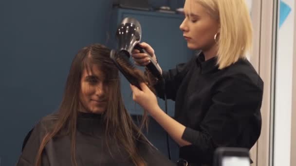 Retrato de mulher feliz no salão de cabeleireiro. Conceito de estilo de cabelo profissional. Cabeleireiro menina secagem cabelo longo usando secador de cabelo e escova. Secagem com secador de sopro — Vídeo de Stock