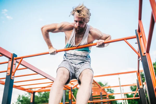 strong athlete doing pull-up on horizontal bar. Muscular man doing pull ups on horizontal bar in park. Gymnastic Bar During Workout. training strongmanoutdoor park gym. Man Doing Exercise gym Outdoor
