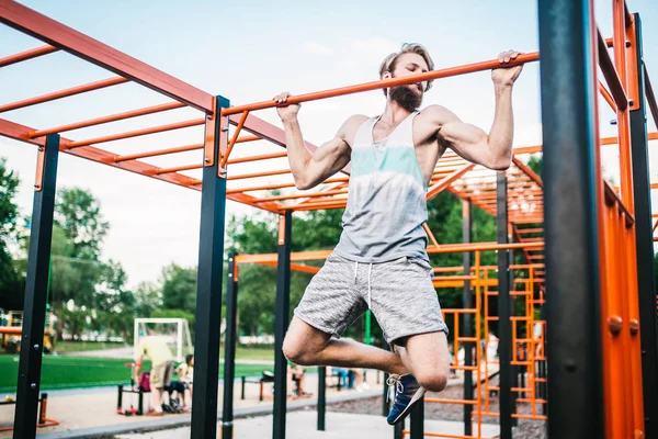 Strong athlete doing pull-up on horizontal bar. Muscular man doing pull ups on horizontal bar in park. Gymnastic Bar During Workout. training strongmanoutdoor park gym. Man Doing Exercise gym Outdoor — Stock Photo, Image