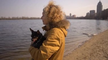 Küçük bir siyah renkli köpek Cins oyuncak terrier tutan yetişkin bir sarışın kıvırcık saç Kafkas kadının Portresi. Eski komik evcil hayvan bir diş köpek dışarı sopalarla, dil değil, doğru bir ısırık düşüyor