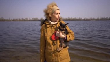 Küçük bir siyah renkli köpek Cins oyuncak terrier tutan yetişkin bir sarışın kıvırcık saç Kafkas kadının Portresi. Eski komik evcil hayvan bir diş köpek dışarı sopalarla, dil değil, doğru bir ısırık düşüyor
