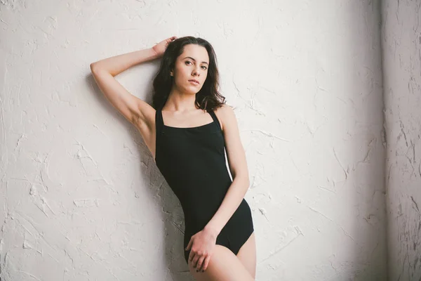 Portrait of young sports woman of athletic build in swimsuit. Woman spend time in a dance studio. Beauty Woman In Sport Wear Stand On Wall. bodysuit posing on wall background. Girl with no makeup — Stock Photo, Image