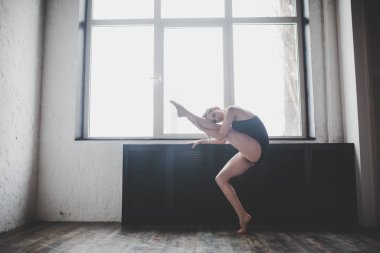 Plastiklik ince kadın pencere yakınında dans. Profesyonel dansçı dans keyfini çıkarın. Lady Dancer Eğitim Modern Bale Sınıfta. Çağdaş dans sanatçısı. Gün ışığı, siluet güzel vücut. Dans teması